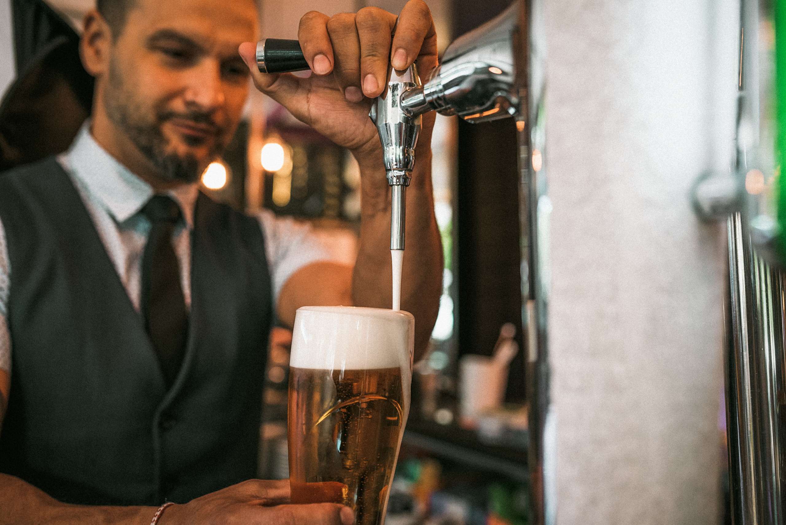 Barman hand at beer tap pouring a draught lager beer serving in a pub.